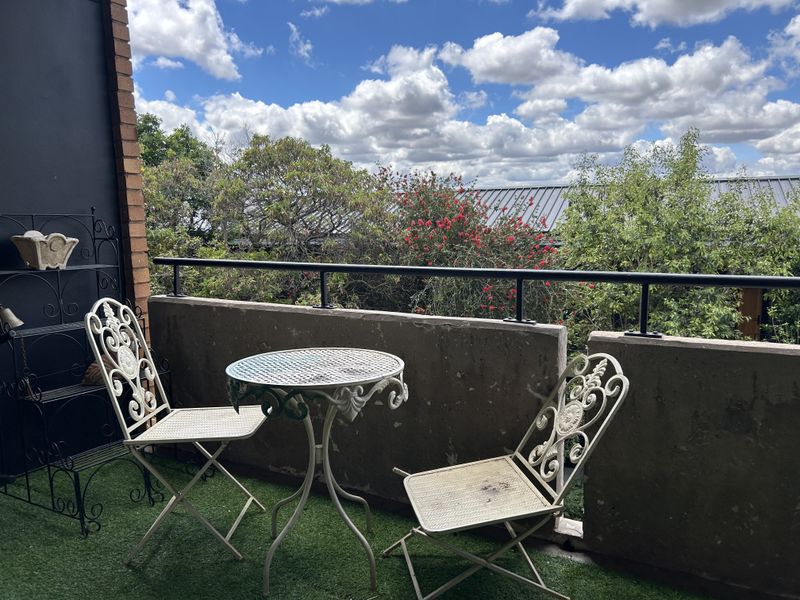 A balcony featuring a concrete balustrade with metal railing, artificial turf flooring, and views of surrounding greenery.