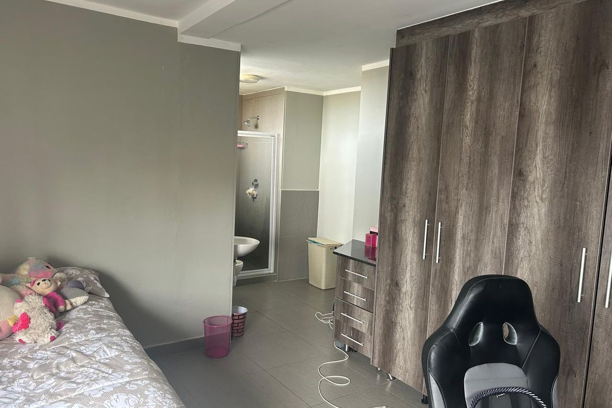 Bedroom featuring built-in wooden cupboards and an attached en-suite bathroom with a shower enclosure and tiled flooring throughout.