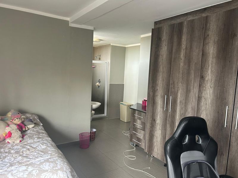 Bedroom featuring built-in wooden cupboards and an attached en-suite bathroom with a shower enclosure and tiled flooring throughout.