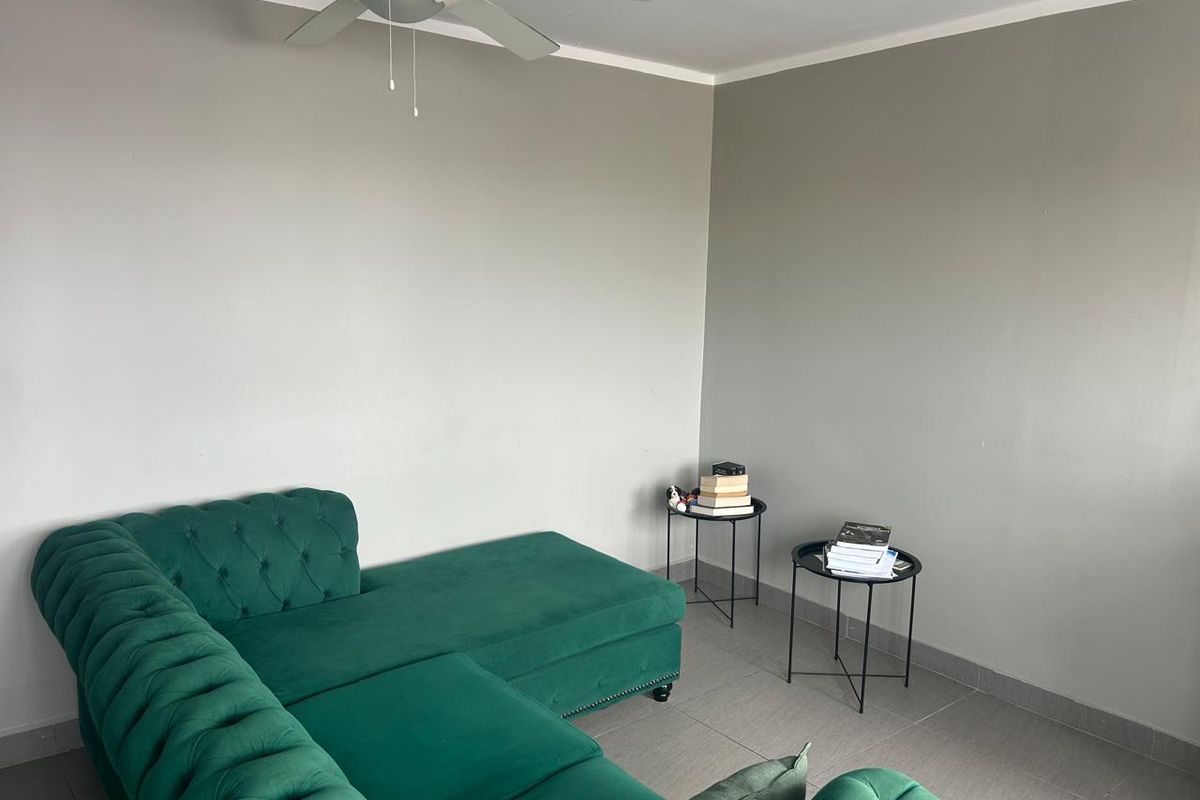 A simple living room area featuring neutral grey walls, tiled flooring, and a ceiling fan.