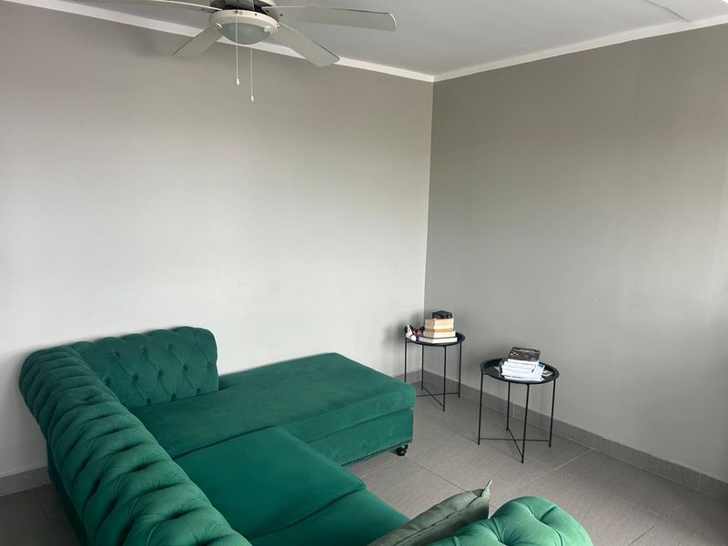 A simple living room area featuring neutral grey walls, tiled flooring, and a ceiling fan.
