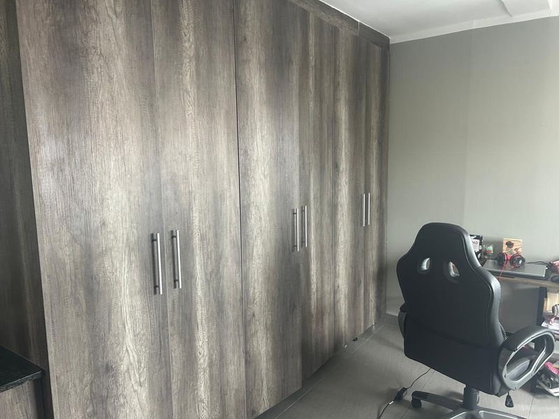 A bedroom featuring modern, full-height built-in cupboards with a wood-grain finish and sleek metal handles.