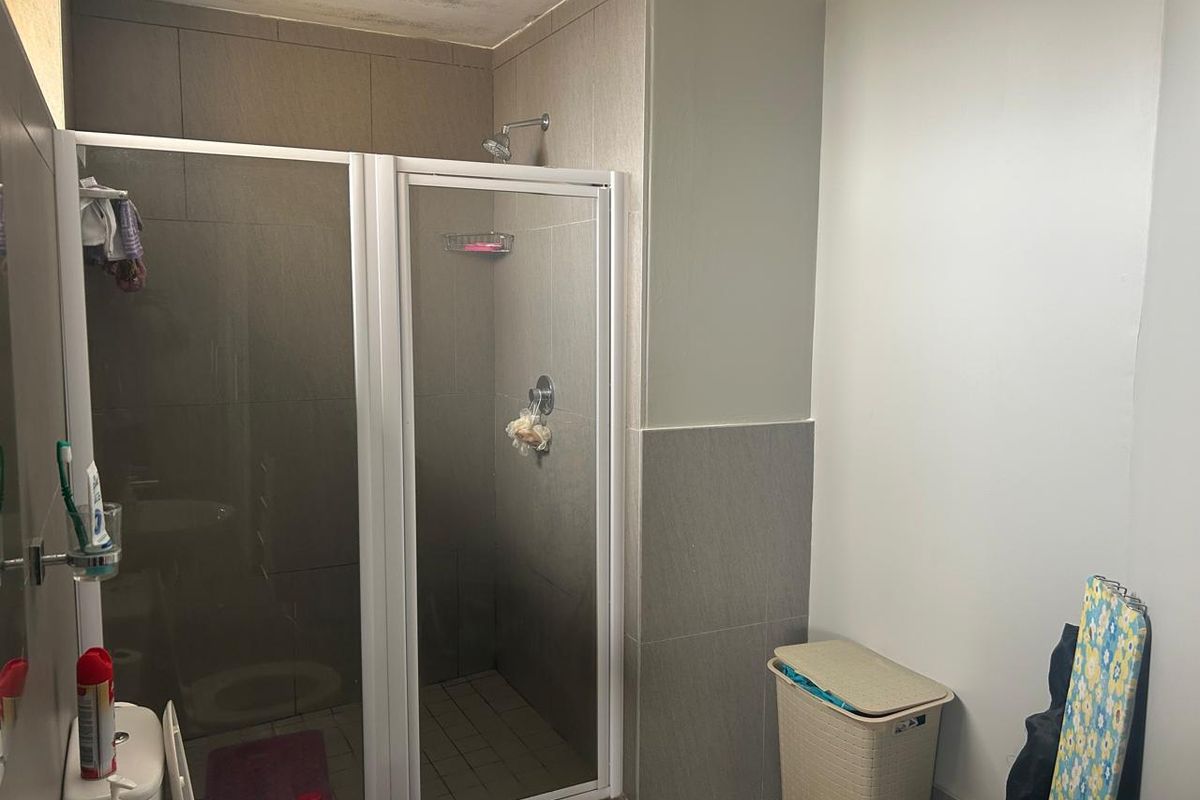 A functional bathroom featuring a glass-enclosed shower, tiled wall finishes, and a standard toilet, with some visible ceiling staining present.