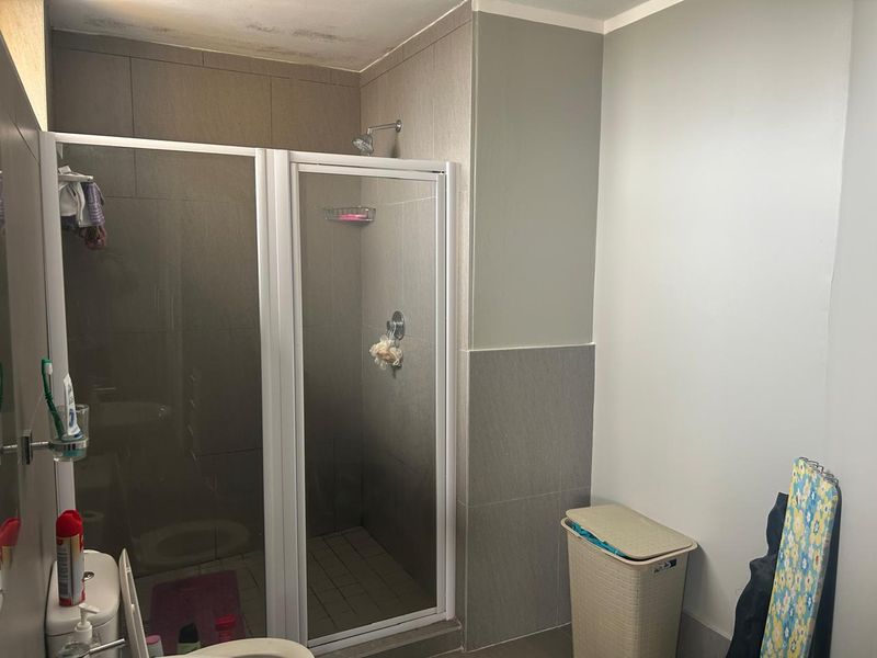 A functional bathroom featuring a glass-enclosed shower, tiled wall finishes, and a standard toilet, with some visible ceiling staining present.
