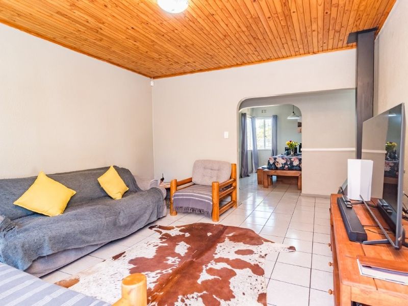 A living room featuring a timber-clad ceiling, tiled flooring, and an archway leading to an adjacent dining area.