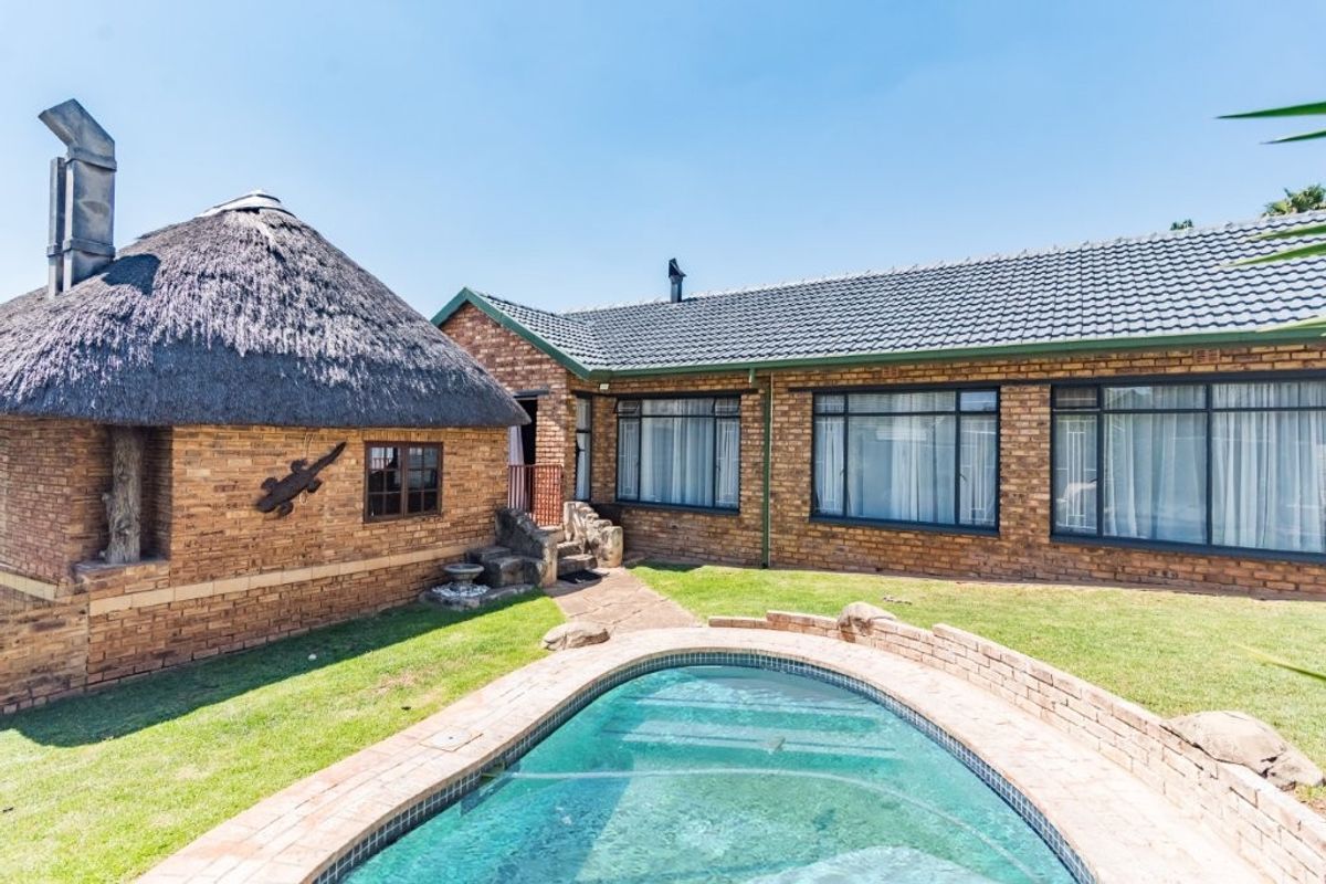 Rear view of the property featuring a swimming pool, a thatched-roof structure, and a brick-built main house with tiled roofing.