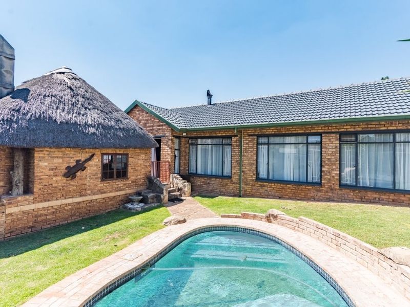 Rear view of the property featuring a swimming pool, a thatched-roof structure, and a brick-built main house with tiled roofing.