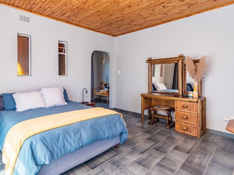 A spacious bedroom featuring a warm timber ceiling, tiled flooring, and an arched doorway leading to an adjoining space.