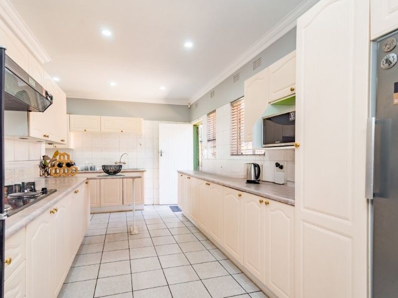 A functional kitchen featuring ample built-in cabinetry, laminate countertops, a gas hob with extractor, and tiled flooring with recessed lighting.