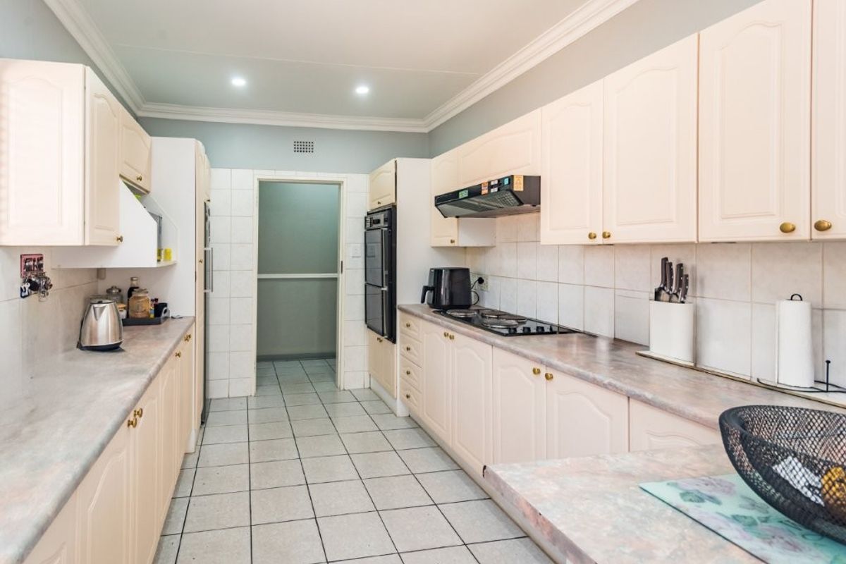 A functional kitchen featuring light-toned cabinetry, laminate countertops, tiled backsplash, and built-in cooking appliances with direct access to an adjacent utility area.
