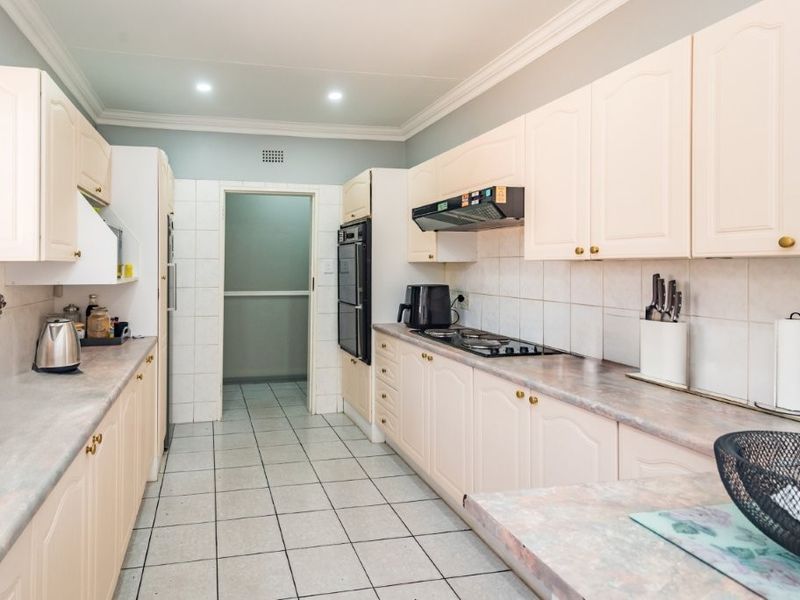 A functional kitchen featuring light-toned cabinetry, laminate countertops, tiled backsplash, and built-in cooking appliances with direct access to an adjacent utility area.