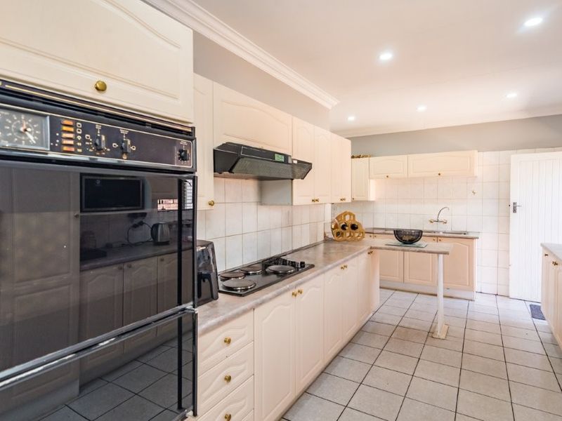 A functional kitchen featuring built-in cabinetry, a hob, an extractor fan, a double oven, and tiled flooring with a neutral backsplash.