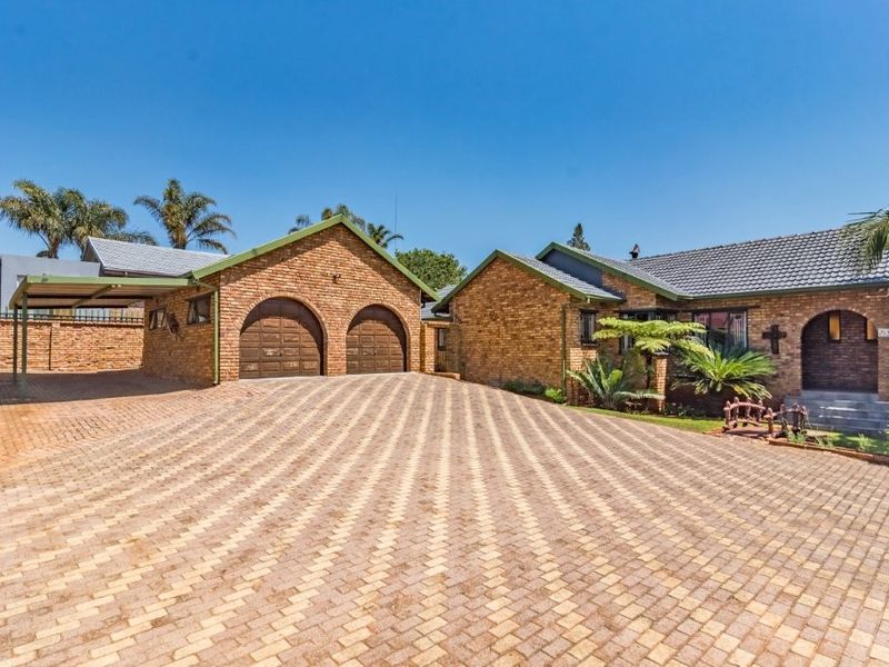 Front view of a brick house featuring a large paved driveway, double garage, attached carport, and an arched entrance.