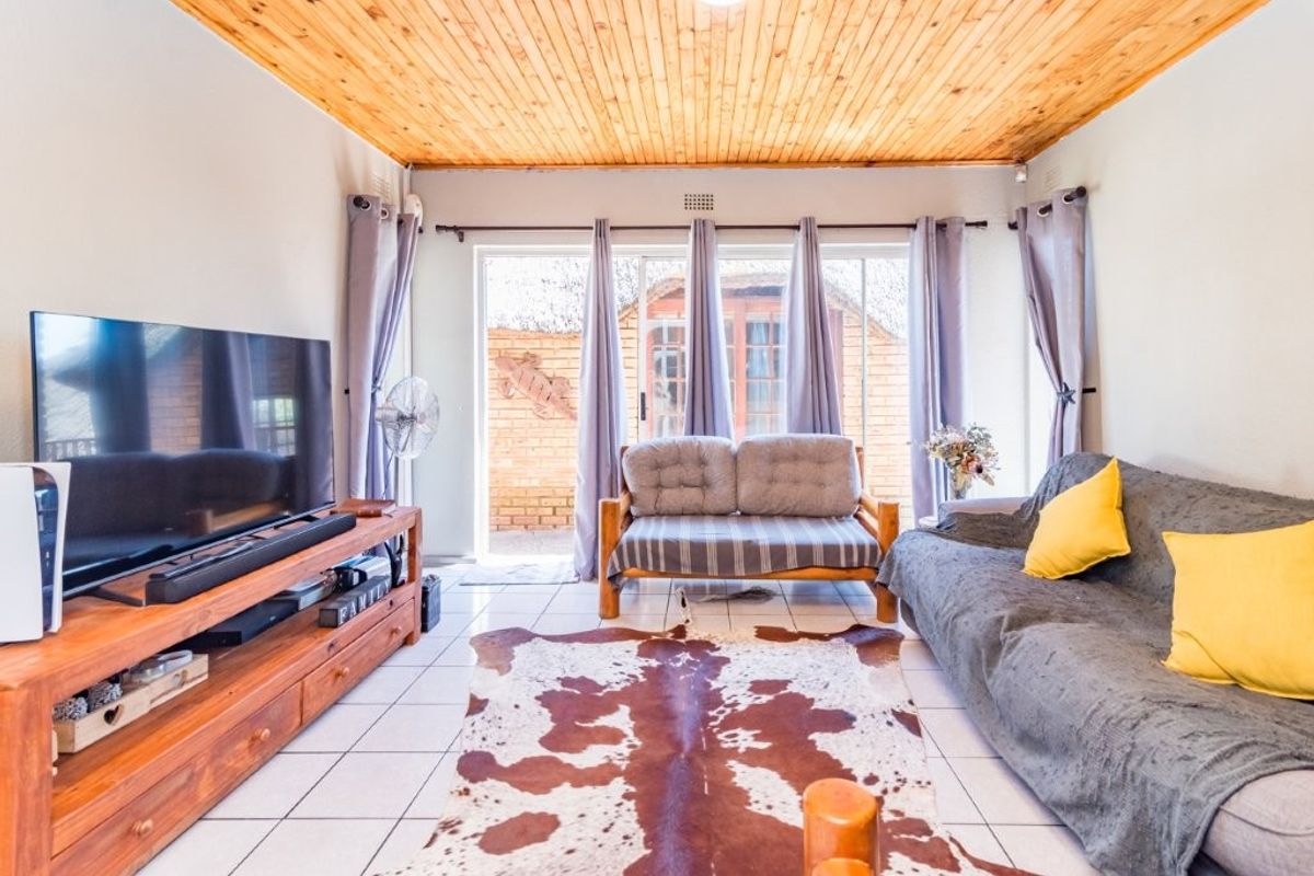 A living room featuring a timber tongue and groove ceiling, tiled flooring, and sliding glass doors providing access to the outdoor area.