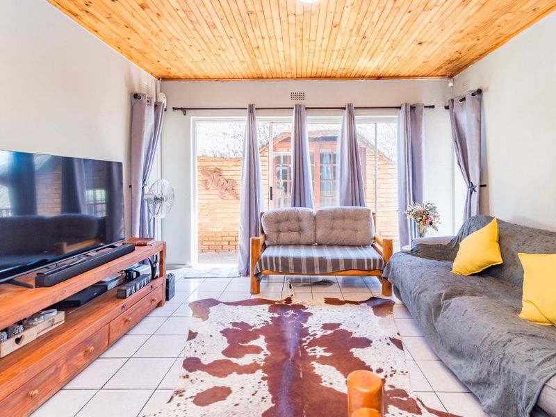 A living room featuring a timber tongue and groove ceiling, tiled flooring, and sliding glass doors providing access to the outdoor area.