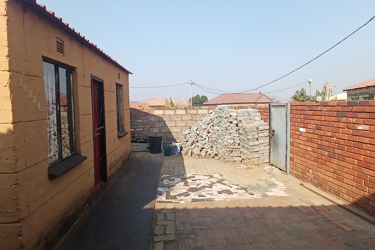 A rear courtyard area featuring a brick boundary wall, paved ground surface, and access to the main structure via a security gate.