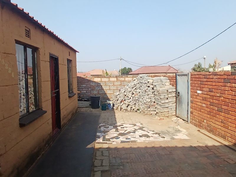 A rear courtyard area featuring a brick boundary wall, paved ground surface, and access to the main structure via a security gate.