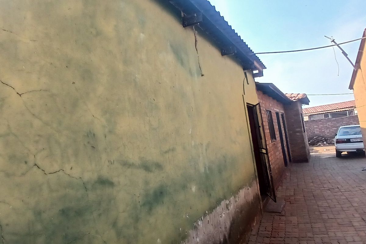 A narrow paved side passage between two residential structures, showing significant wear to the exterior wall plaster and paint.