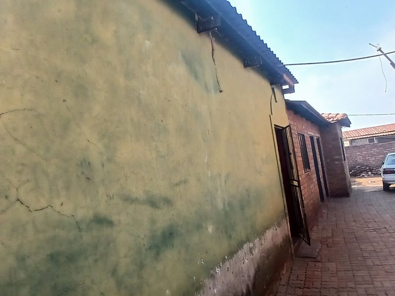 A narrow paved side passage between two residential structures, showing significant wear to the exterior wall plaster and paint.