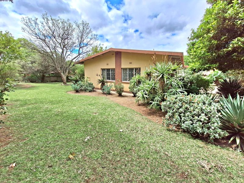 A view of the rear elevation of the house featuring a well-maintained garden with established shrubs and trees.