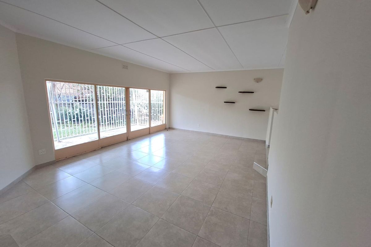 A spacious, empty living room featuring neutral tiled flooring, a drop ceiling, and large sliding glass doors with security gates leading to the exterior.