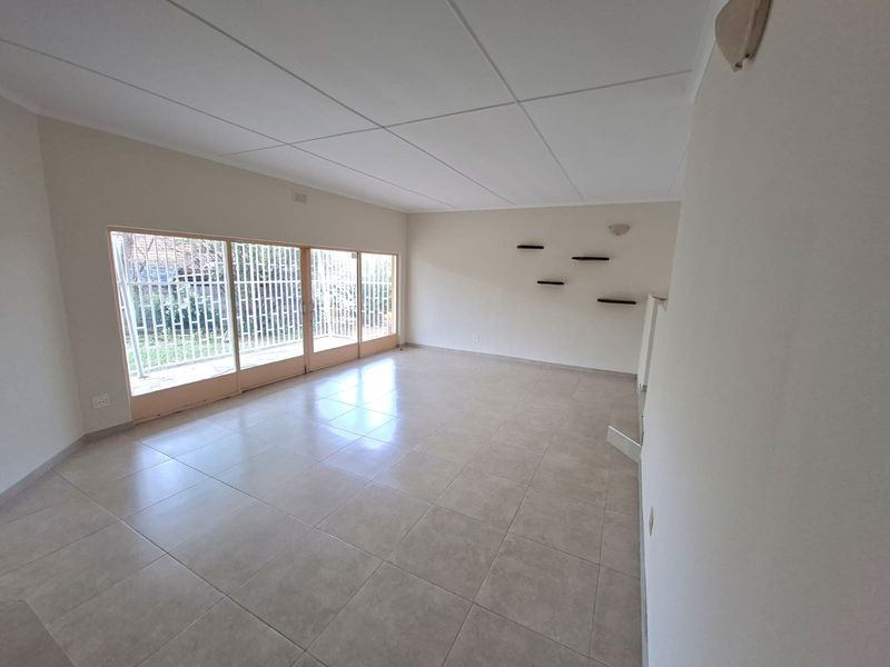 A spacious, empty living room featuring neutral tiled flooring, a drop ceiling, and large sliding glass doors with security gates leading to the exterior.