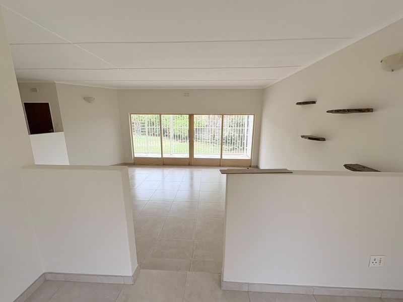 A bright, open-plan living area featuring neutral tiled flooring, a partition wall, and large sliding glass doors providing access to the garden.