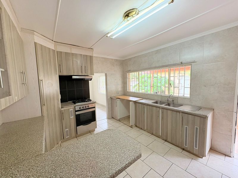 A functional kitchen featuring light wood-grain cabinetry, granite countertops, a double basin sink, and built-in cooking appliances with tiled finishes throughout.
