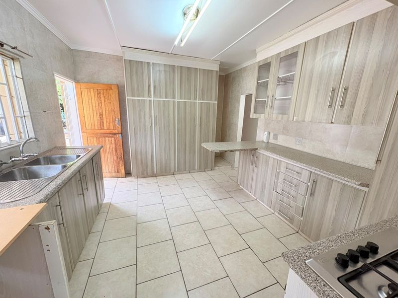 Spacious kitchen featuring extensive built-in cabinetry, granite countertops, a double basin sink, and a gas hob with neutral tiled flooring throughout.