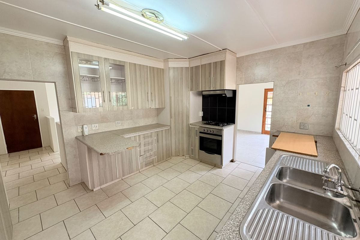 A functional kitchen featuring light wood-grain cabinetry, tiled splashbacks, a double stainless steel sink, and a built-in stove with an extractor fan.