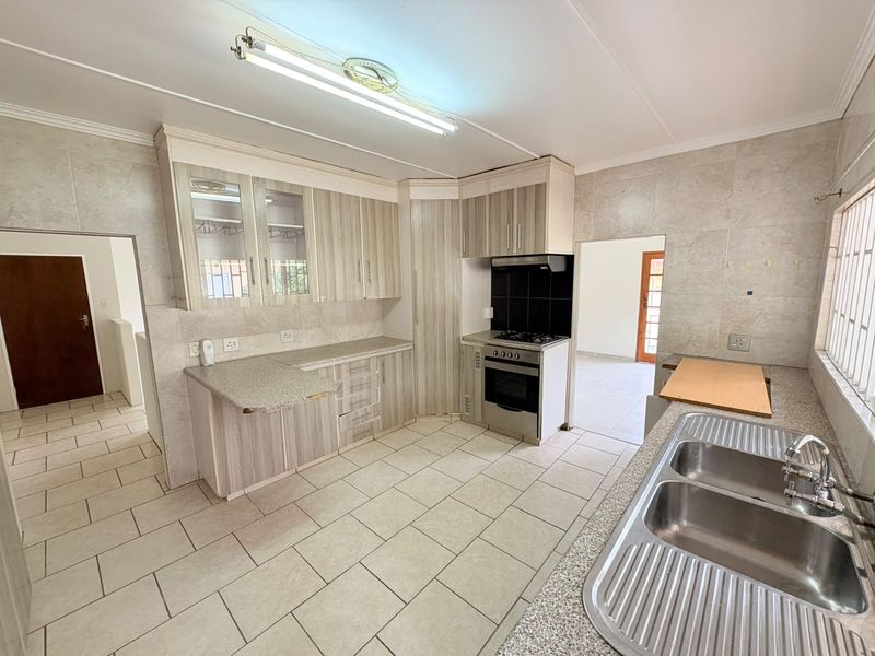 A functional kitchen featuring light wood-grain cabinetry, tiled splashbacks, a double stainless steel sink, and a built-in stove with an extractor fan.