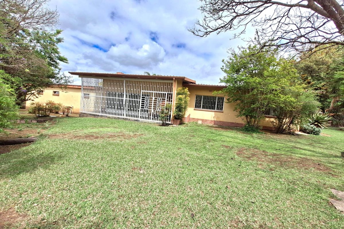 Rear view of the house featuring a covered patio area, security bars on windows, and a spacious garden with mature trees.