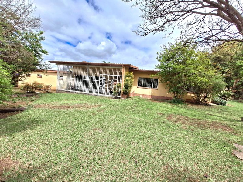 Rear view of the house featuring a covered patio area, security bars on windows, and a spacious garden with mature trees.