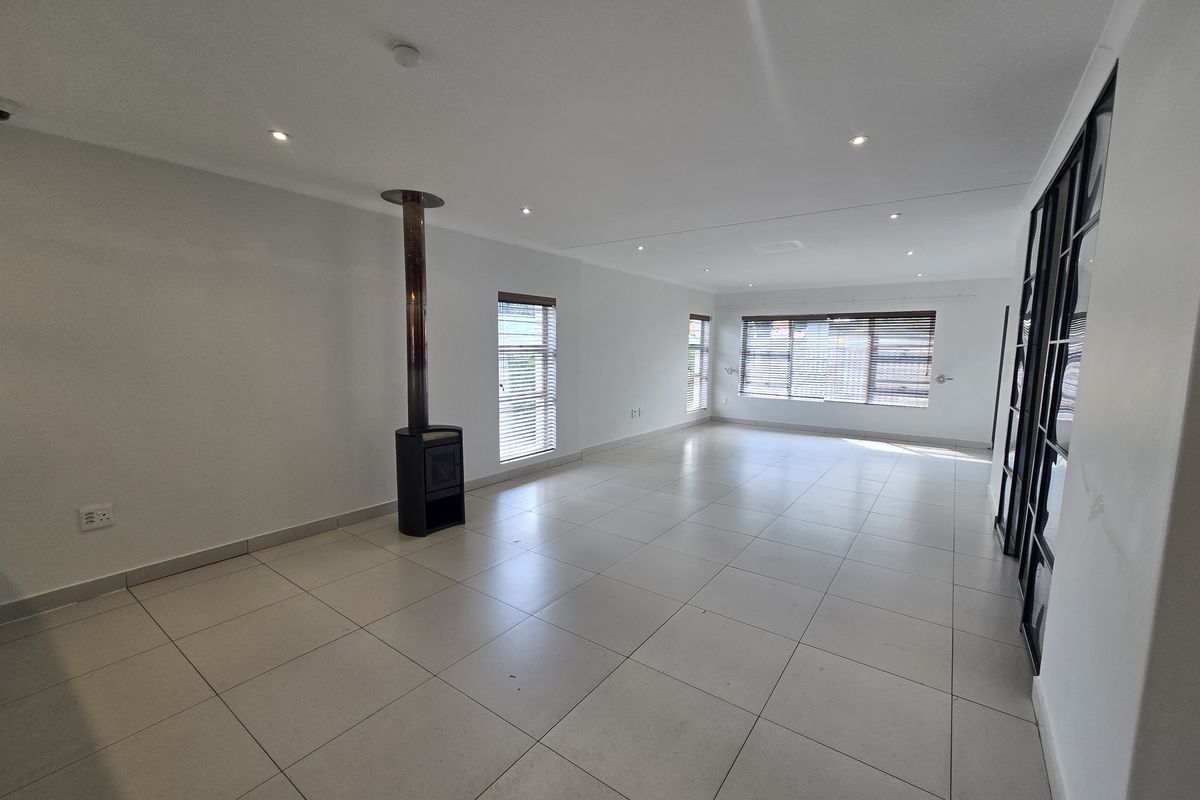 Spacious, light-filled living area featuring neutral tiled flooring, a modern freestanding fireplace, and sleek black-framed glass partitions.