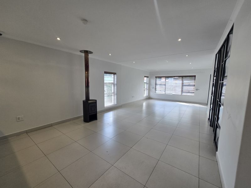 Spacious, light-filled living area featuring neutral tiled flooring, a modern freestanding fireplace, and sleek black-framed glass partitions.
