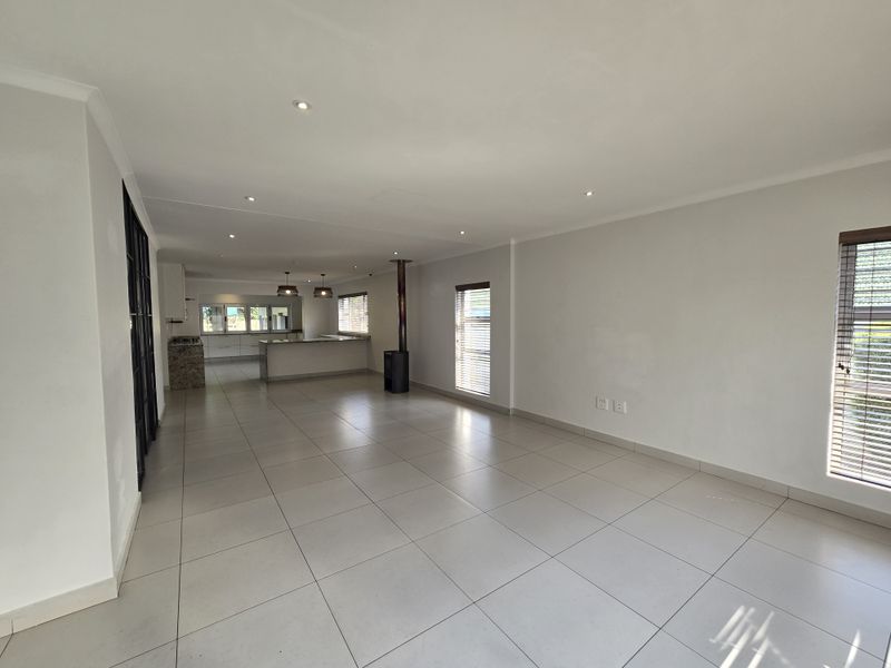 Spacious open-plan living and kitchen area featuring neutral tiled flooring, recessed lighting, a modern freestanding fireplace, and a functional kitchen island.