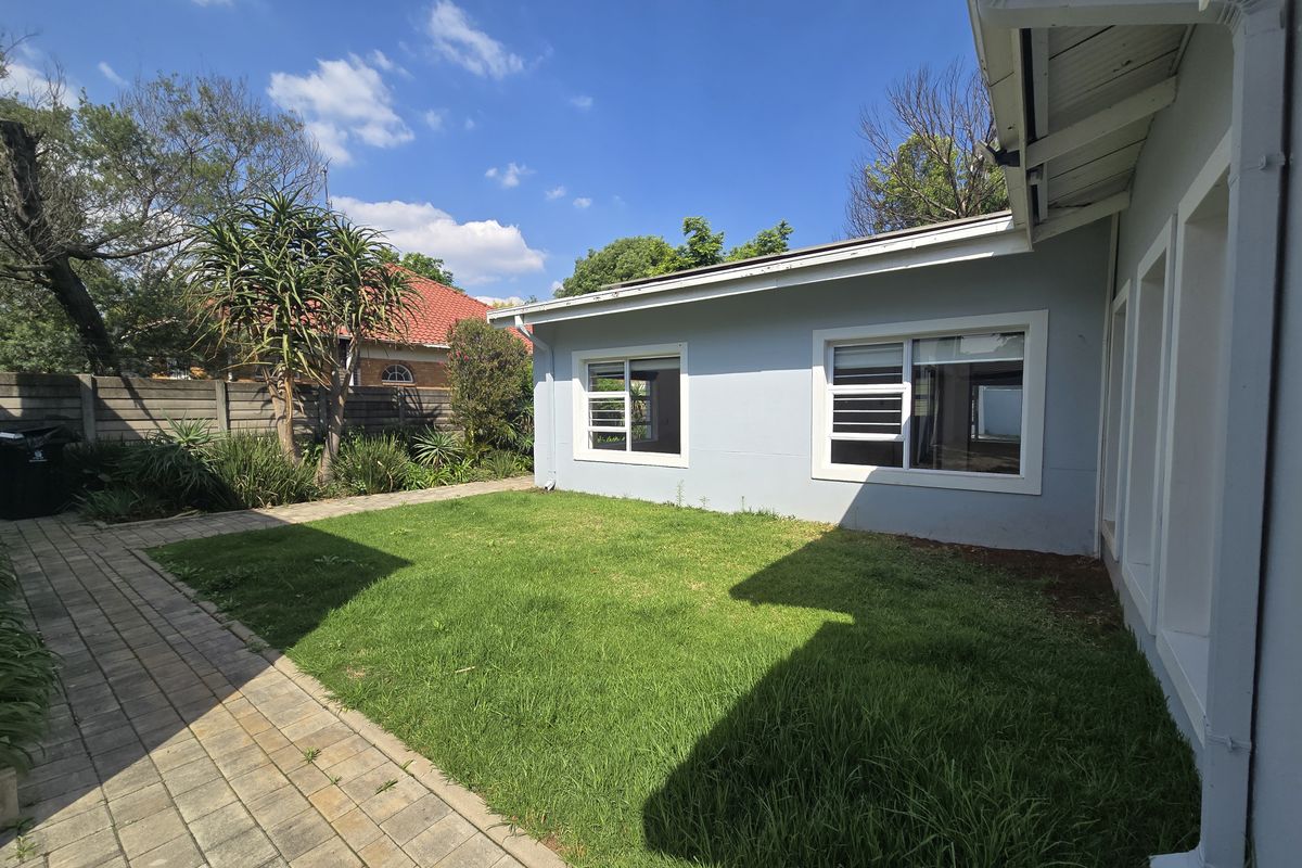 A rear exterior view of the property featuring a paved walkway, a small lawn, and sliding windows set against a boundary wall.