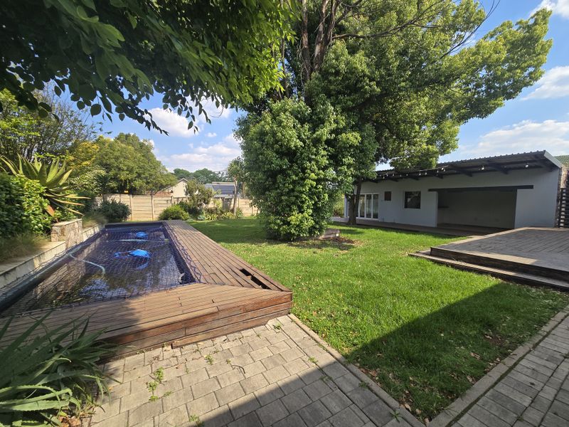 Spacious backyard featuring a swimming pool with timber decking, a paved patio area, and a covered outdoor entertainment space set within a landscaped garden.