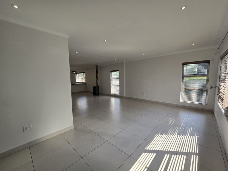Spacious open-plan living area featuring neutral tiled flooring, recessed downlights, and a modern freestanding fireplace, offering a bright and versatile layout.