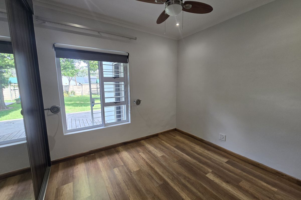 A bright, empty bedroom featuring laminate flooring, a ceiling fan, and a built-in sliding door wardrobe with a view of the garden.