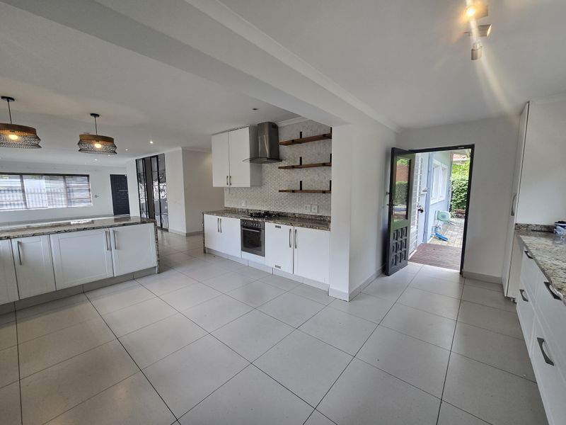 Spacious open-plan kitchen featuring modern white cabinetry, granite countertops, built-in appliances, and tiled flooring with direct access to the outdoor patio area.