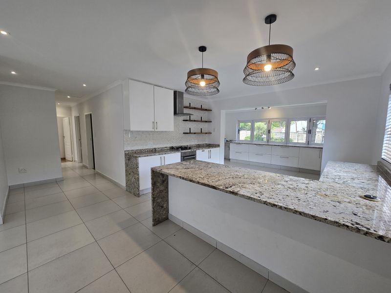 Modern kitchen featuring granite countertops, ample built-in cabinetry, a built-in oven with extractor fan, and tiled flooring in an open-plan layout.