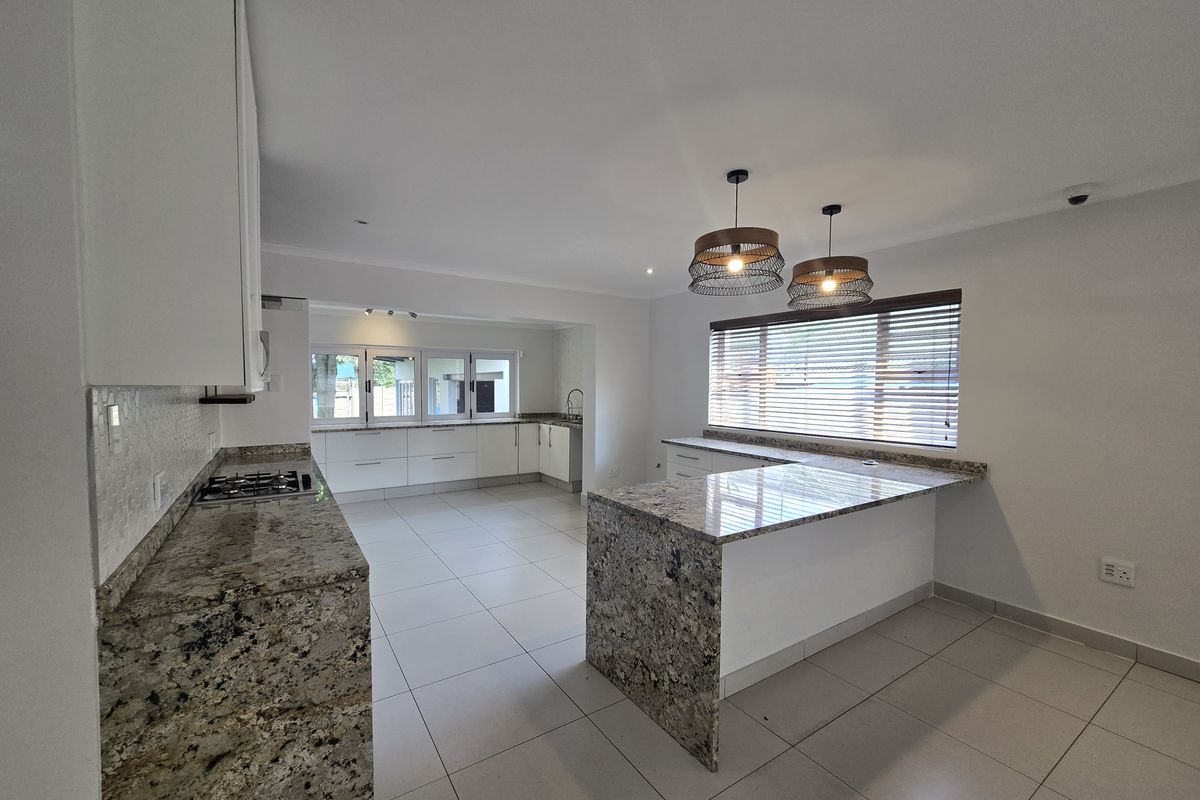 Spacious modern kitchen featuring granite countertops, ample white cabinetry, a built-in gas hob, and large floor tiles in an open-plan layout.