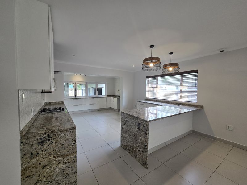Spacious modern kitchen featuring granite countertops, ample white cabinetry, a built-in gas hob, and large floor tiles in an open-plan layout.