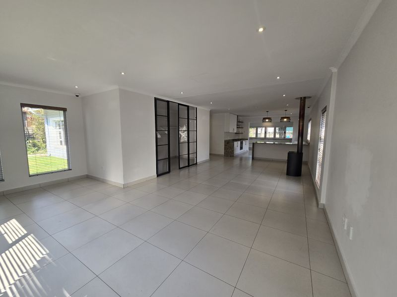 Spacious open-plan living and kitchen area featuring large format floor tiles, a modern fireplace, and a sleek black-framed glass partition.