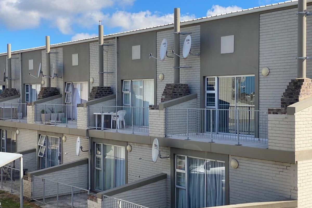 Rear elevation of a multi-story apartment complex featuring private balconies with metal railings, sliding glass doors, and brick exterior finishes.