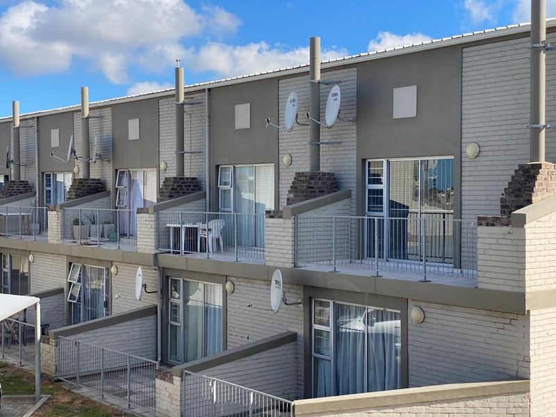Rear elevation of a multi-story apartment complex featuring private balconies with metal railings, sliding glass doors, and brick exterior finishes.