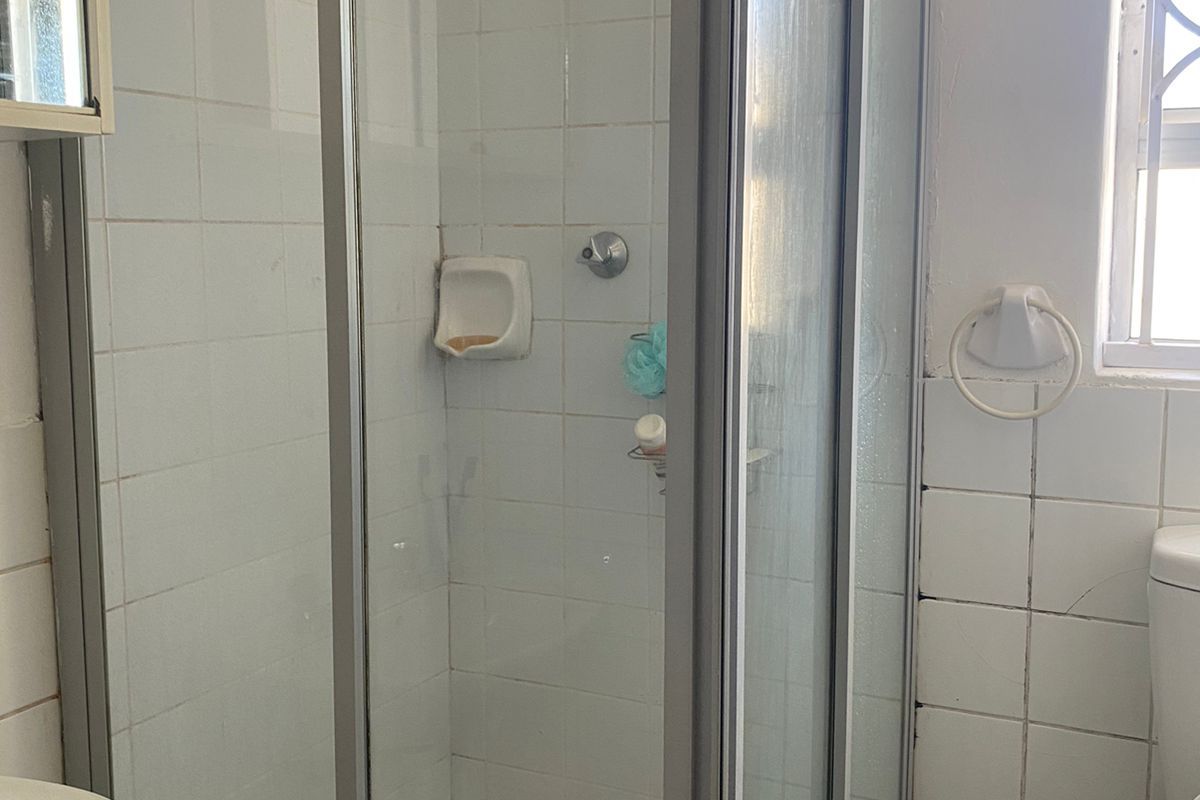 A functional bathroom featuring a glass-enclosed shower with a rain shower head, tiled walls, and a window for natural light.