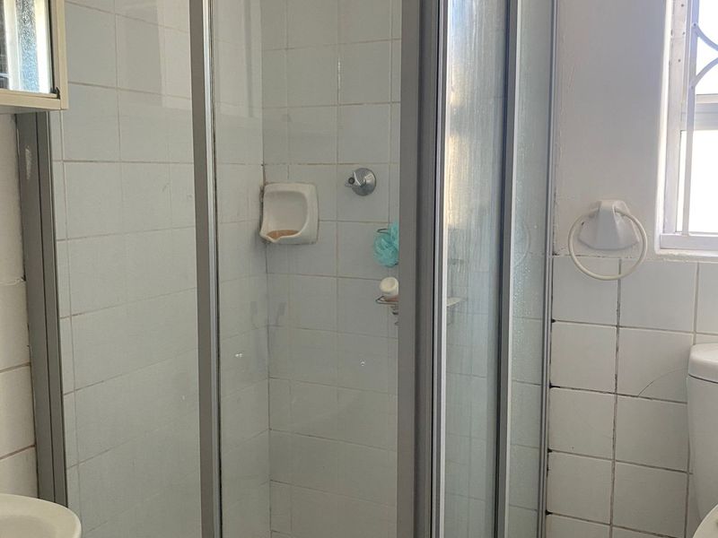 A functional bathroom featuring a glass-enclosed shower with a rain shower head, tiled walls, and a window for natural light.