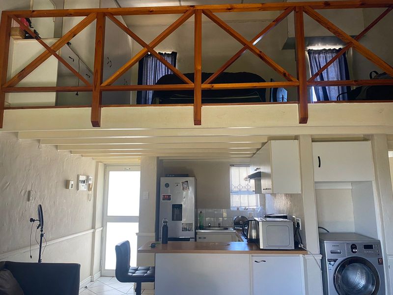 Open plan apartment living area featuring a mezzanine level with wooden balustrade, compact kitchen with built-in cabinetry, and dedicated laundry space.